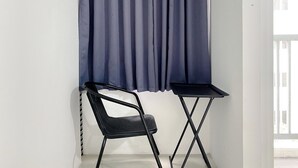 Una stanza d'angolo con una sedia nera e un tavolino piccolo contro un muro bianco, con una tenda blu parzialmente tirata.