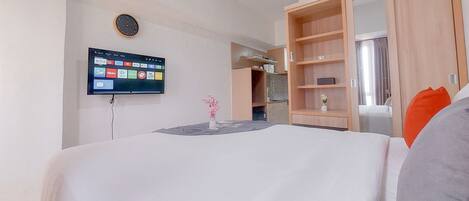 A hotel room with a bed, a TV mounted on the wall, a wardrobe, and a small table with a vase.
