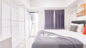 A modern hotel room with a large bed, a wardrobe, and a window with curtains. - Good Place And Homey 1Br At Tamansari Bintaro Mansion Apartment (South Tangerang)