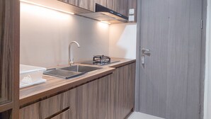 A modern kitchen with wooden cabinetry, a stainless steel sink, and a built-in oven. - Good Place And Homey 1Br At Tamansari Bintaro Mansion Apartment (South Tangerang)