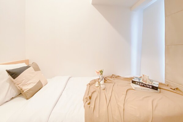 A neatly made bed with a beige blanket, a pillow, and a book titled "PERFUME" on top.
