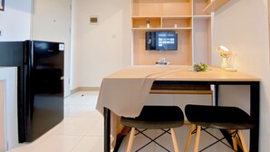 A modern kitchen with a black refrigerator, a wooden table with a white tablecloth, two black chairs, and a mounted TV on the wall. - Good And Cozy Stay 2Br Tokyo Riverside Pik 2 Apartment (Teluknaga)