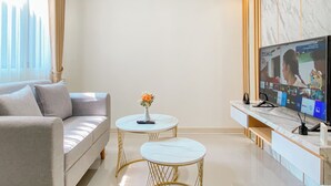 A modern living room with a sofa, two round tables, a TV, and a marble wall. - Comfort 2Br Apartment At Meikarta Cikarang (Cikarang)