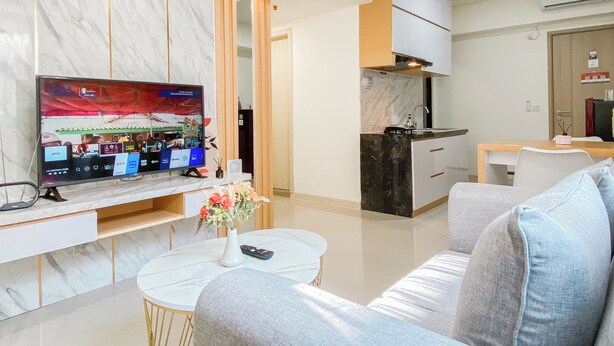 A modern living room with a flat-screen TV, a coffee table with a vase, and a sofa. - Comfort 2Br Apartment At Meikarta Cikarang (Cikarang)