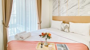 A hotel room with a neatly made bed, a vase with flowers, a tray with a cup and a bottle, and a marble wall. - Comfort 2Br Apartment At Meikarta Cikarang (Cikarang)