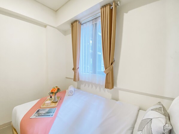 A hotel room with a bed, a window with curtains, a bedside table with a vase of flowers, and a picture frame.