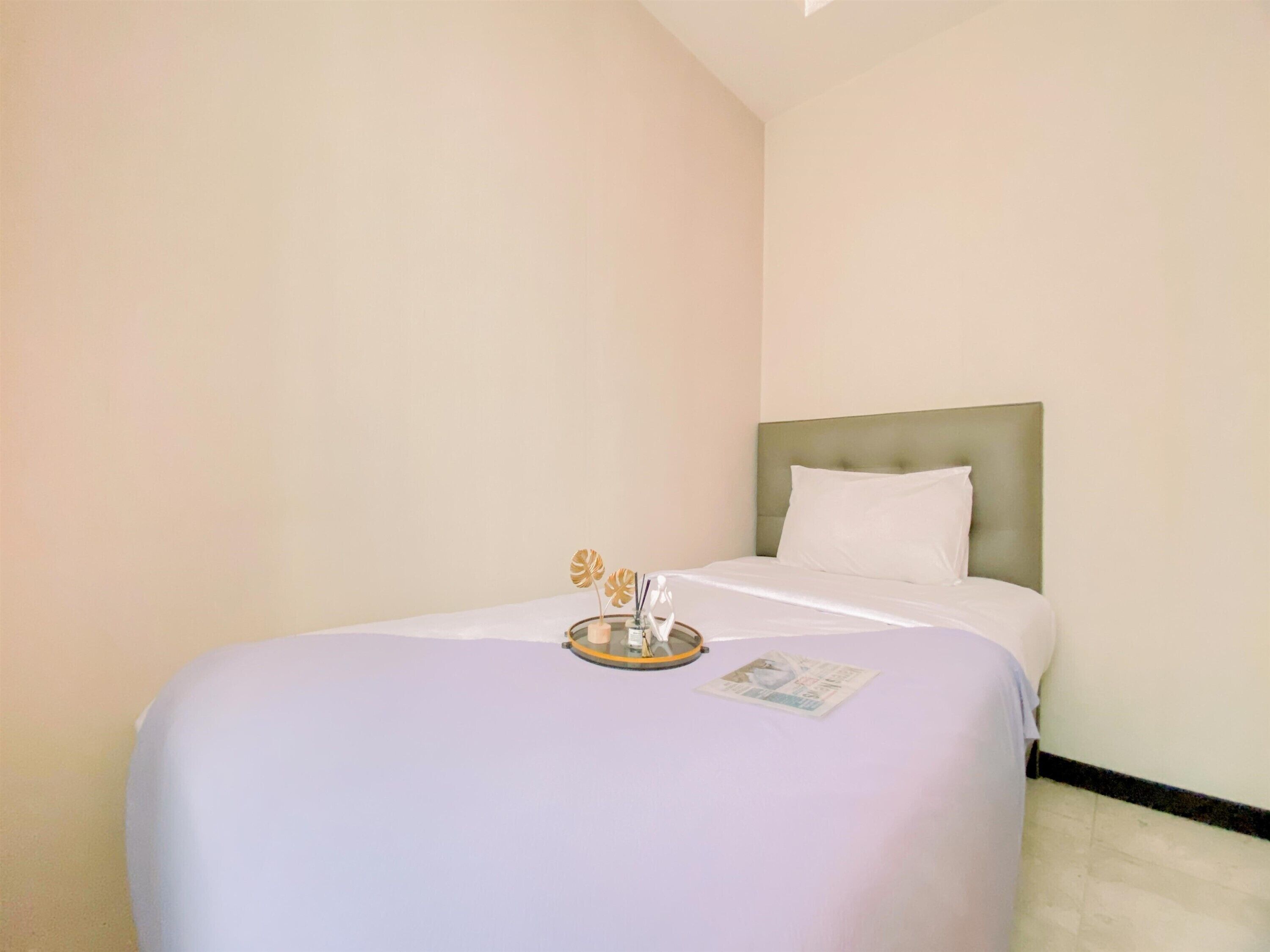A hotel room with a single bed, a headboard, and a small table with a tray and candles.