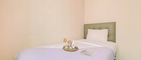 A hotel room with a single bed, a headboard, and a small table with a tray and candles.
