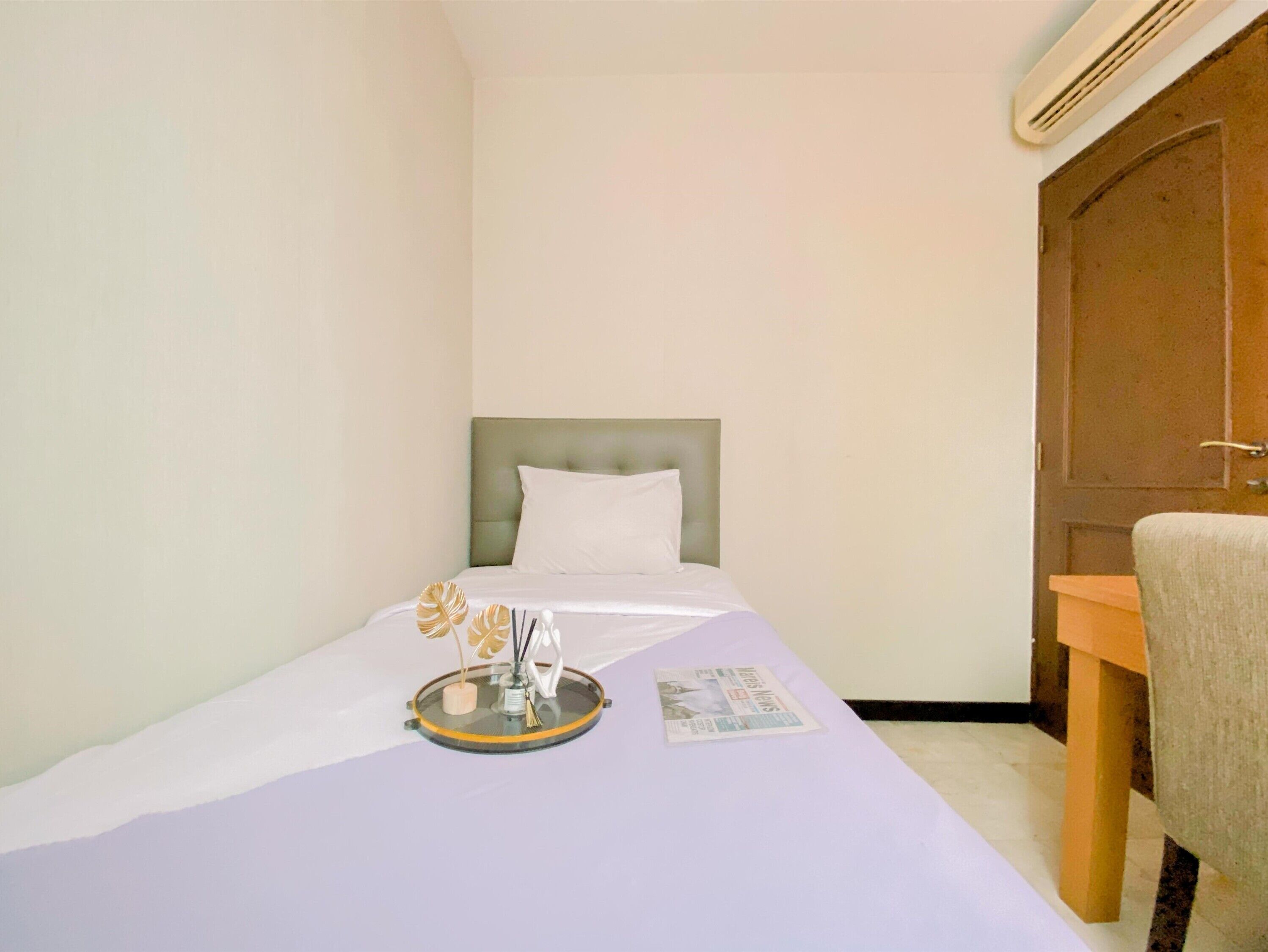 A small, neatly arranged bedroom with a single bed, a bedside table, a chair, and a door.
