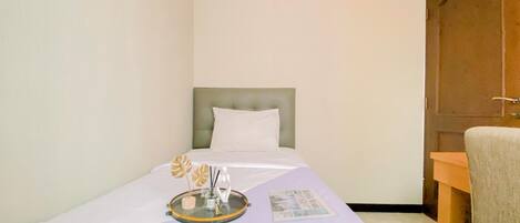A small, neatly arranged bedroom with a single bed, a bedside table, a chair, and a door.