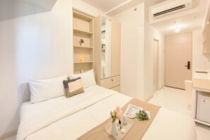 A modern hotel room with a neatly made bed, a small table with a vase and flowers, a built-in wardrobe, and a bathroom with a mirror and sink. - Simply And Enjoy Living Studio At Tokyo Riverside Pik 2 Apartment (Teluknaga)