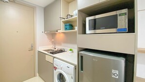 Een kleine keuken met een magnetron, een kleine koelkast, een wasmachine en een fornuis.