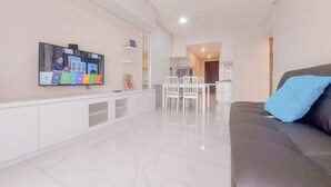 Ein modernes Wohnzimmer mit einem an der Wand befestigten Flachbildfernseher, einem braunen Ledersofa mit blauem Kissen und einem weißen Essbereich mit Stühlen.