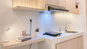 Een moderne keuken met houten kastjes, een wit aanrecht, een inbouwafzuigkap, een spoelbak en een klein werkblad met bureaulamp en boeken.