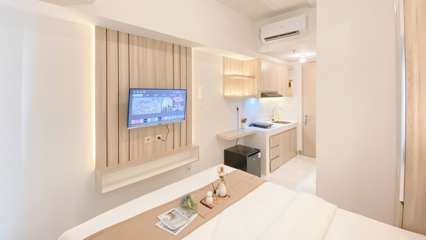 Een moderne hotelkamer met een bed, een aan de muur bevestigde televisie, een kleine kitchenette en een badkamer die door een geopende deur zichtbaar is.