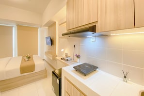 A modern hotel room with a bed, a small kitchenette, and a TV mounted on the wall. - Cozy Living Apartment Studio At Tokyo Riverside Pik 2 (Teluknaga)