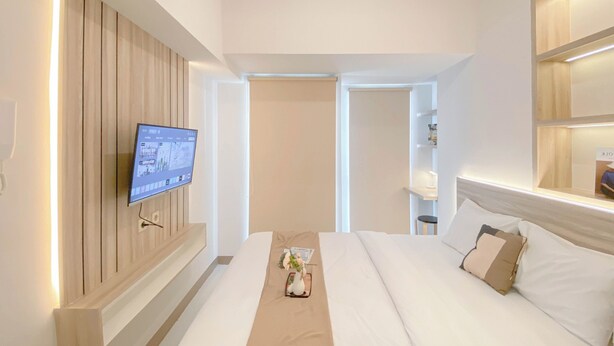 Ein modernes Hotelzimmer mit einem großen Bett, einem an der Wand montierten Flachbildfernseher und einem Nachttisch mit Blumenvase.