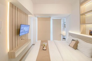 Ein modernes Hotelzimmer mit einem großen Bett, einem an der Wand montierten Flachbildfernseher und einem Nachttisch mit Blumenvase.