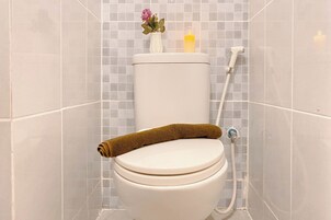 A toilet with a brown towel, a vase with flowers, and a candle on the tank.