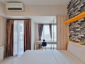 Et hotelværelse med seng, skrivebord, stol, spejl og aircondition.