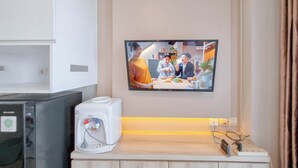 Une chambre d’hôtel dotée d’un téléviseur à écran plat fixé au mur, d’un mini-bar avec distributeur d’eau et d’un meuble en bois en dessous.