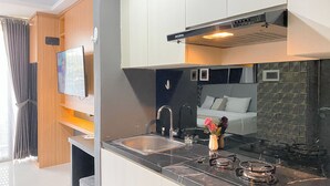 A modern kitchen with a built-in stove, a sink, and a flat-screen TV mounted on the wall. - Homey And Cozy Living Studio At West Vista Apartment (Jakarta)