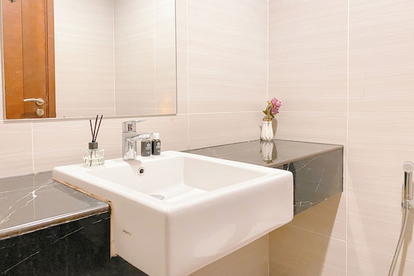 Un baño con lavamanos blanco, un espejo y un florero con flores.
