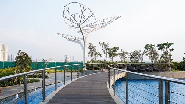 A modern outdoor pool area with a wooden deck, metal railings, and a unique metal sculpture. - Homey And Cozy Living Studio At West Vista Apartment (Jakarta)