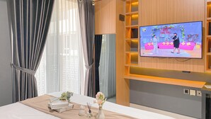 A hotel room with a bed, a TV mounted on the wall, and a window with curtains. - Homey And Cozy Living Studio At West Vista Apartment (Jakarta)