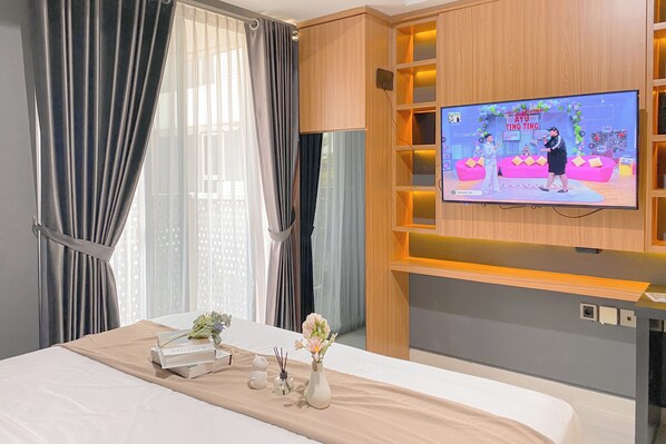 Une chambre d’hôtel avec un lit, un téléviseur fixé au mur et une fenêtre avec des rideaux.