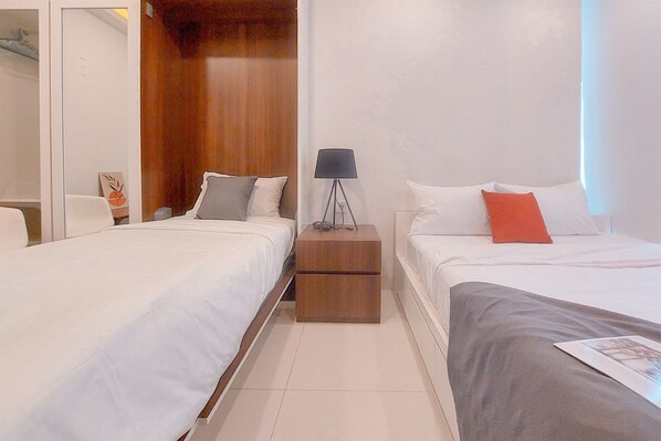 Two single beds with white bedding and red accents, a nightstand, and a wardrobe.