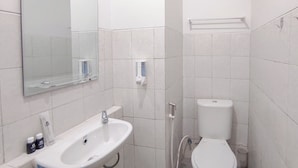 A small, modern bathroom with a white sink, toilet, and mirror. - Homey Studio With Easy Pool Access Apartment At Suncity Residence (Sidoarjo)