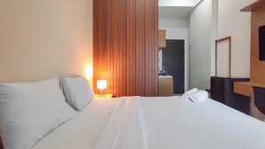 A hotel room with a bed, a nightstand, a lamp, a mirror, and a wooden panel wall. - Homey Studio With Easy Pool Access Apartment At Suncity Residence (Sidoarjo)
