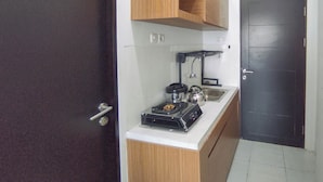 A compact kitchen with a stove, kettle, and sink. - Homey Studio With Easy Pool Access Apartment At Suncity Residence (Sidoarjo)