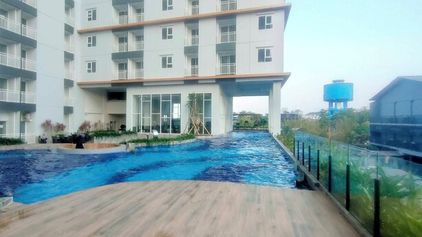 A modern building with a swimming pool, a covered area, and a water tower in the background. - Homey Studio With Easy Pool Access Apartment At Suncity Residence (Sidoarjo)