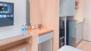 A modern hotel room with a wooden desk, a flat-screen TV, a minibar, and a built-in washer and dryer. - Good Place Studio At Urbantown Serpong Apartment (South Tangerang)