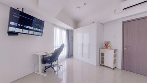 A modern, well-lit room with a flat-screen TV mounted on the wall, a desk with a chair, a wardrobe, and a small cabinet. - Comfortable And Homey 1Br Tamansari Bintaro Mansion Apartment (South Tangerang)