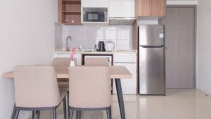 A modern kitchen with a stainless steel refrigerator, microwave, and kettle. There is a dining table with four chairs. - Comfortable And Homey 1Br Tamansari Bintaro Mansion Apartment (South Tangerang)