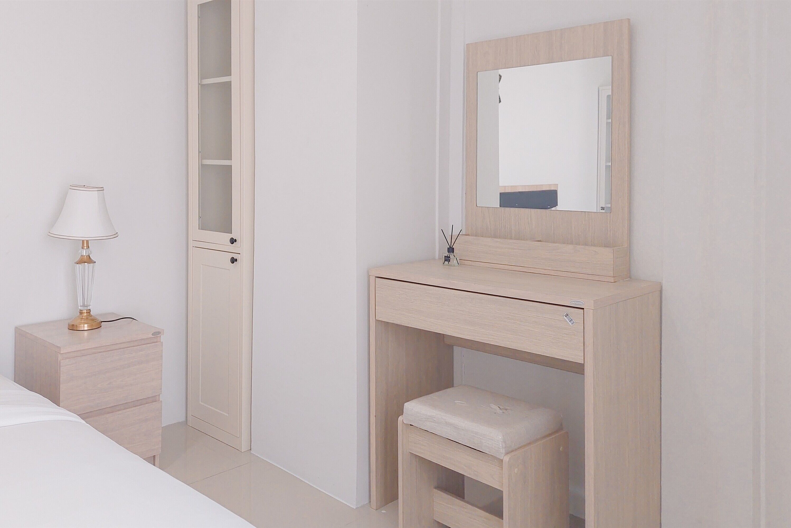 A minimalist bedroom with a bed, bedside table, lamp, wardrobe, and a mirror.