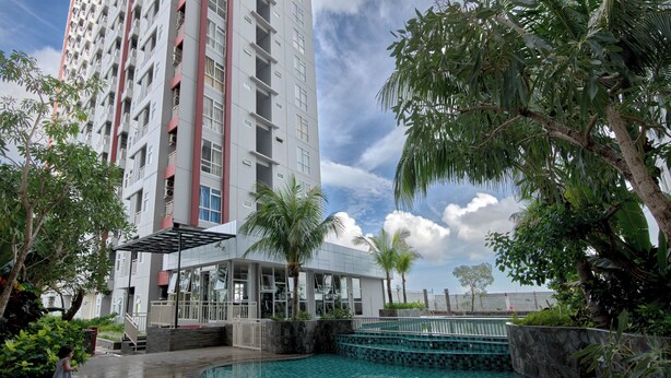 A modern hotel with a rooftop pool, surrounded by lush greenery and a tall building in the background. - Comfort Studio Room At Vida View Apartment (Makassar)