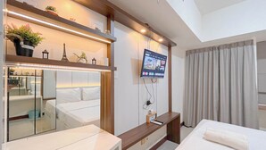 A modern hotel room with a bed, a TV mounted on the wall, a small table, and a mirror. - Comfort Studio Room At Vida View Apartment (Makassar)