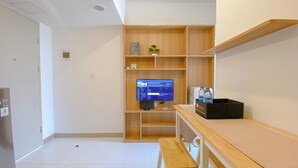 A hotel room with a wooden desk, a television displaying news, a small plant, and a water dispenser. - Cozy Living 2Br Apartment At Tokyo Riverside Pik 2 (Teluknaga)