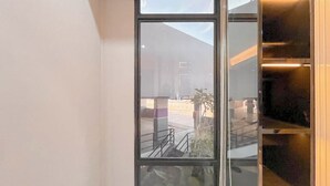 Une vue à travers une fenêtre ornée d’une rambarde en métal, avec un escalier et la façade d’un immeuble.
