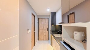 Un couloir étroit avec une porte en bois, un coin cuisine comprenant un évier et une machine à café, ainsi qu’un plan de travail.