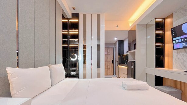 Une chambre d’hôtel moderne dotée d’un grand lit, d’un téléviseur fixé au mur et d’un coin cuisine séparé.