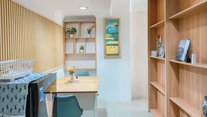 A room with a wooden desk, a blue chair, a shelf with plants, a framed painting, and a wooden bookshelf.