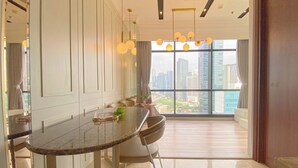 Un espace de salle à manger moderne avec une table en verre, des chaises et des luminaires suspendus. On peut apercevoir un paysage urbain à travers de grandes fenêtres.