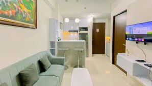 A modern living room with a light blue sofa, a white coffee table, and a TV mounted on the wall. - Good Place And Homey 2Br At Transpark Cibubur Apartment Near Mall (Depok)