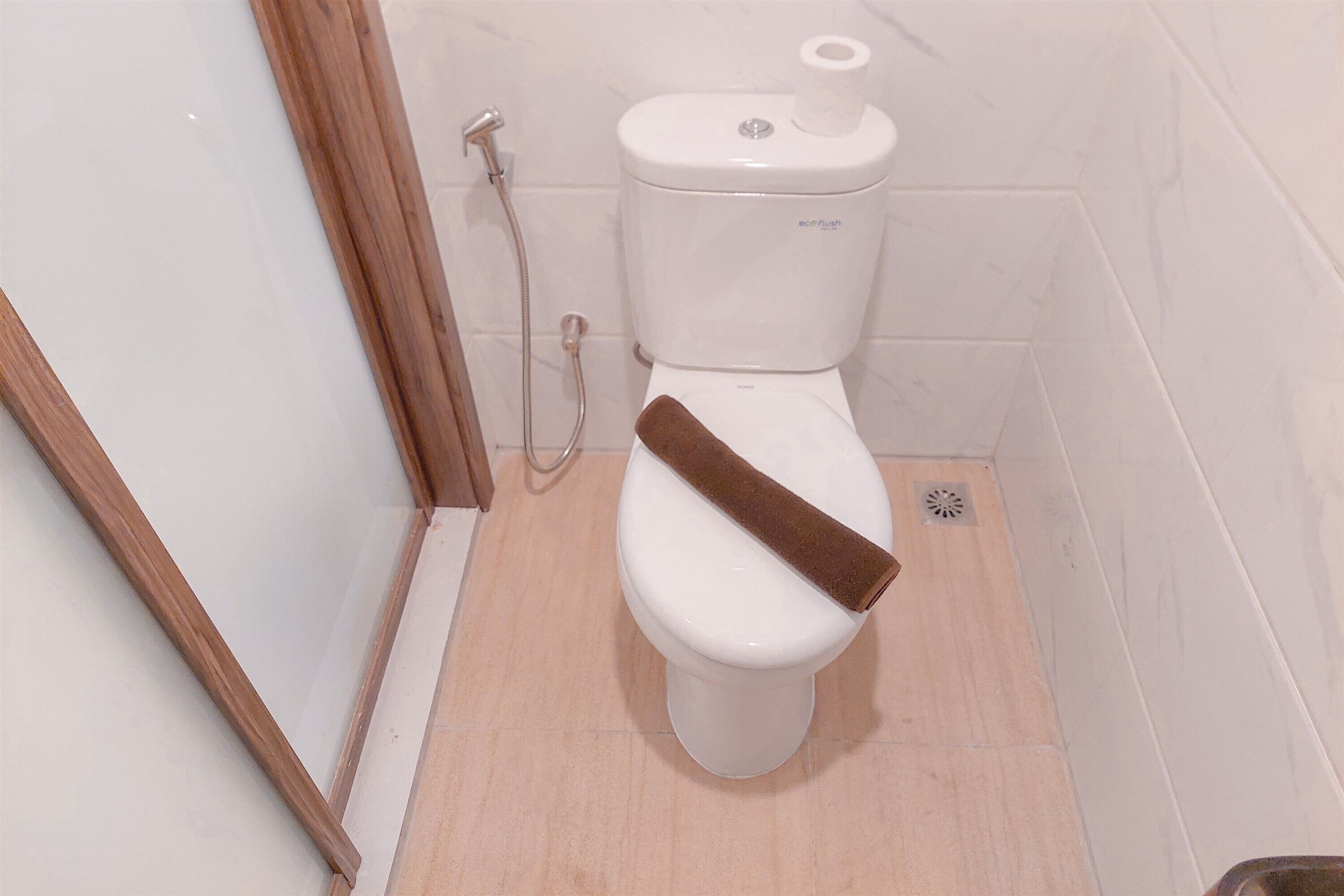 Un inodoro blanco con una toalla marrón encima, un dispensador de papel higiénico y un cabezal de ducha.