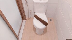 Eine weiße Toilette mit einem braunen Handtuch, einem Toilettenpapierhalter und einem Duschschlauch.